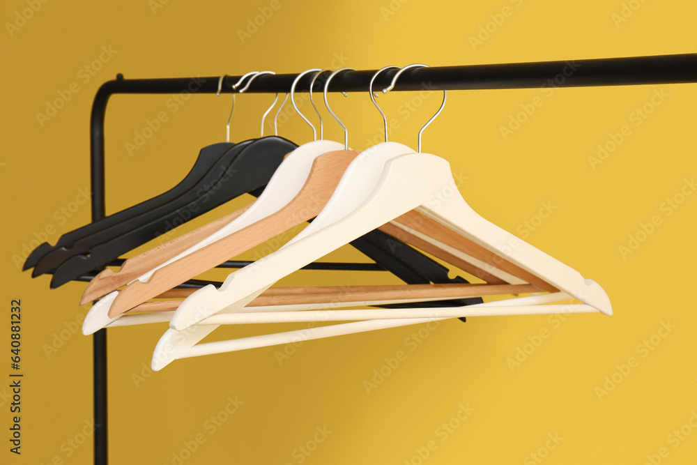 Rack with wooden clothes hangers on yellow background