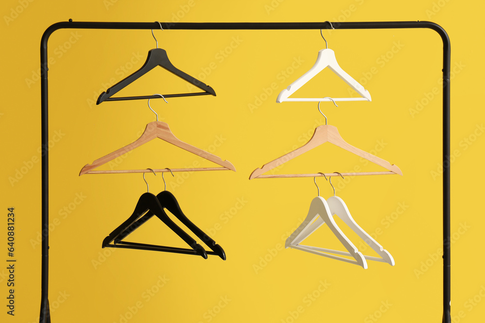 Rack with wooden clothes hangers on yellow background