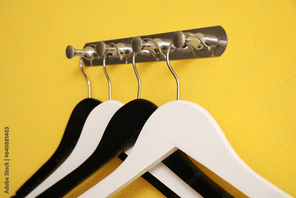 Rack with wooden clothes hangers on yellow background