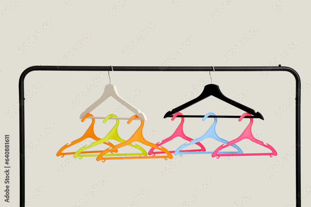 Rack with plastic clothes hangers on grey background