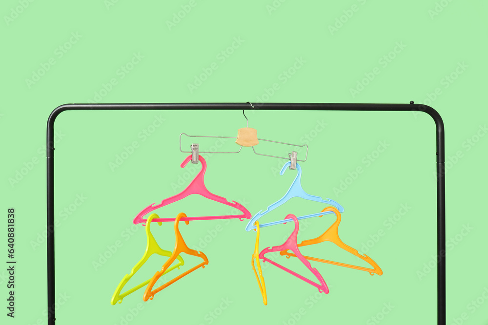 Rack with plastic clothes hangers on green background