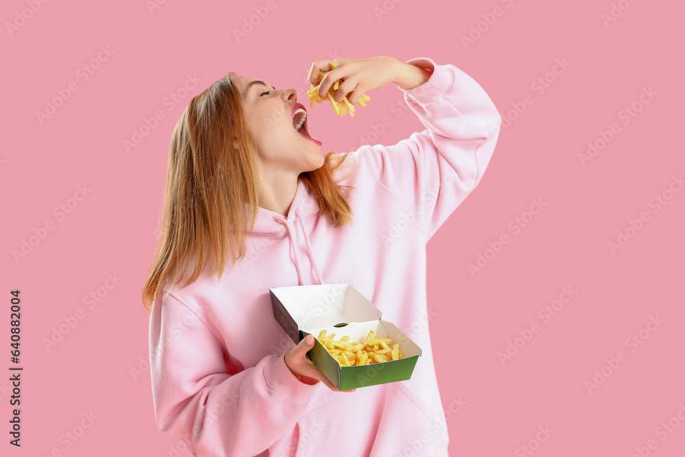 Beautiful young woman eating french fries on pink background