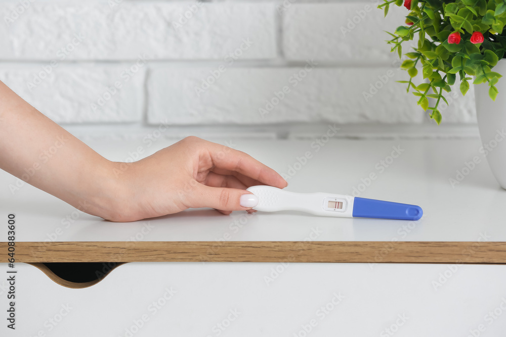 Female hand with positive pregnancy test on light table, closeup