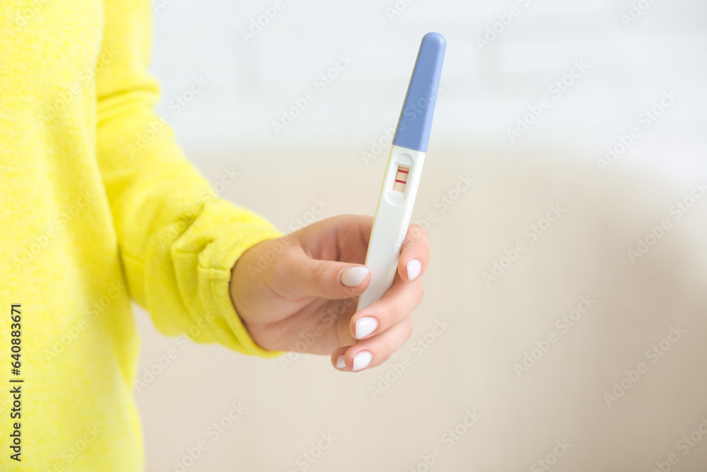 Female hand with positive pregnancy test against blurred background, closeup