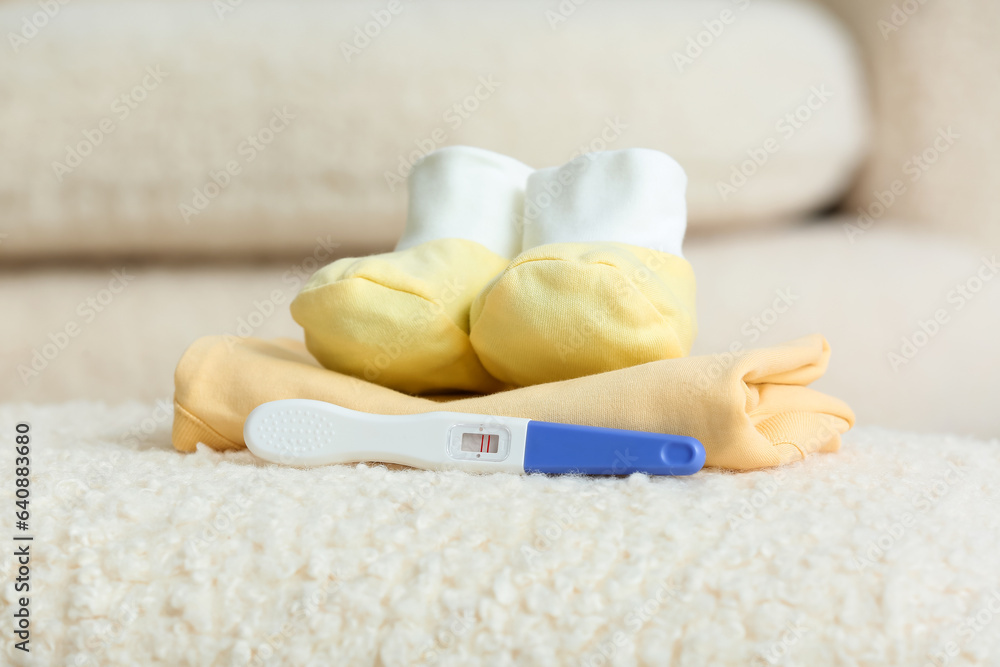 Positive pregnancy test, baby booties and clothes on sofa