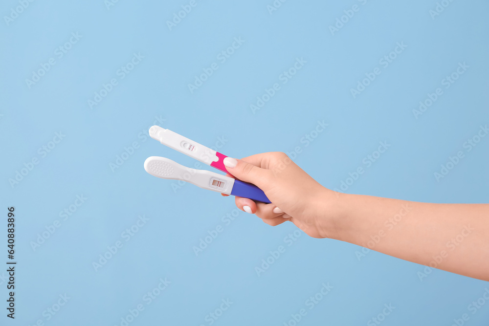 Female hand with positive pregnancy tests on color background