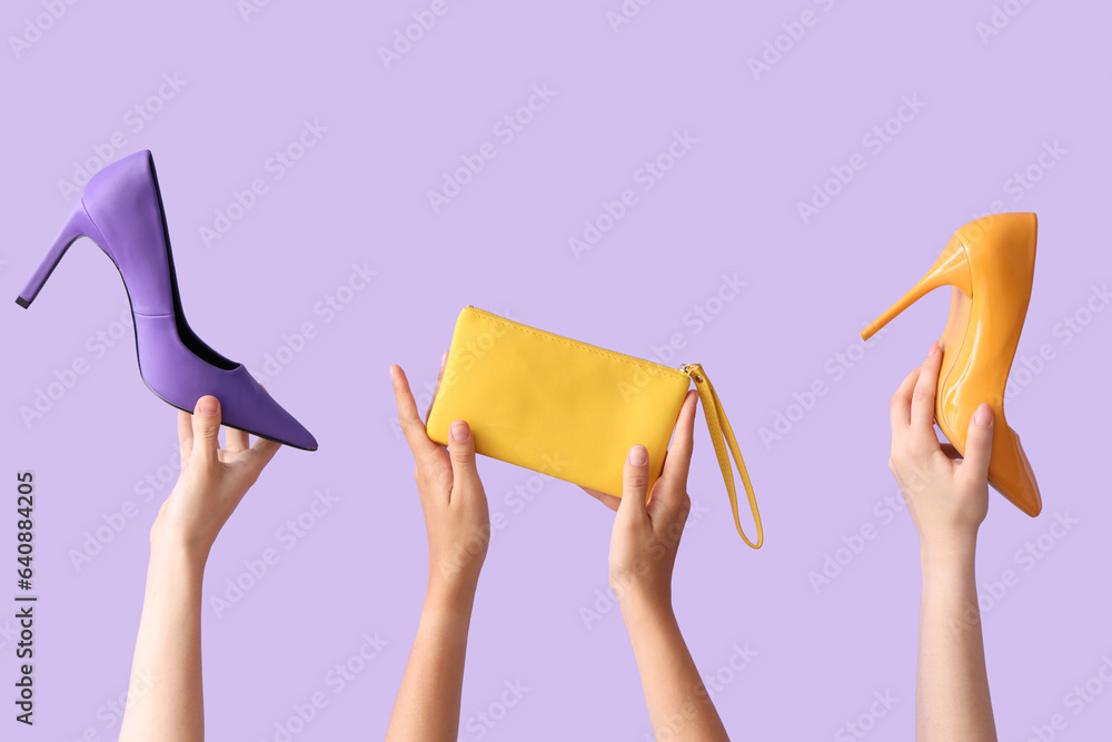 Female hands holding different stylish bags and high heels on lilac background