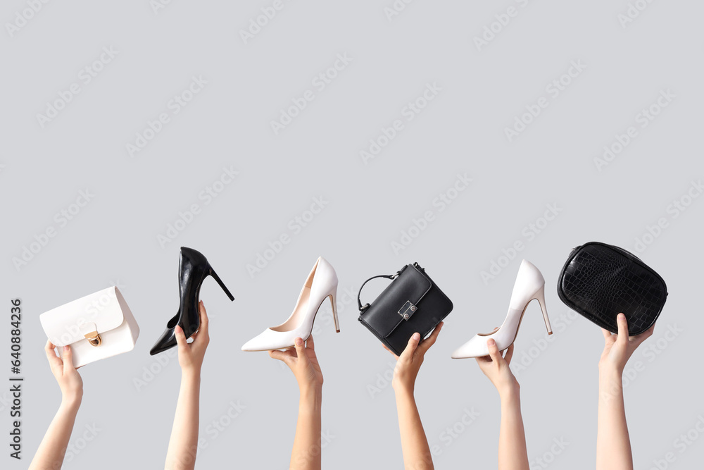 Female hands holding different stylish bags and high heels on grey background