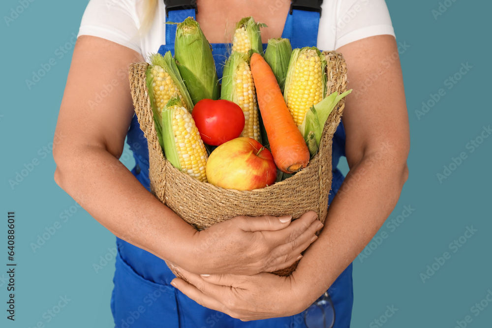 Mature female farmer with wicker basket full of different ripe vegetables on blue background