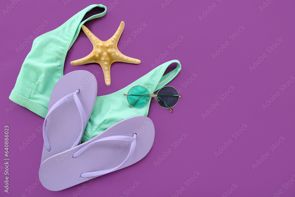 Pair of flip flops with swimsuit and sunglasses on purple background