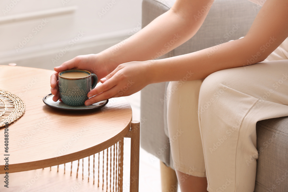 Woman taking cup of tasty coffee from table at home