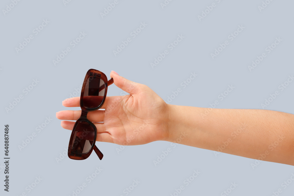 Woman holding stylish sunglasses on grey background