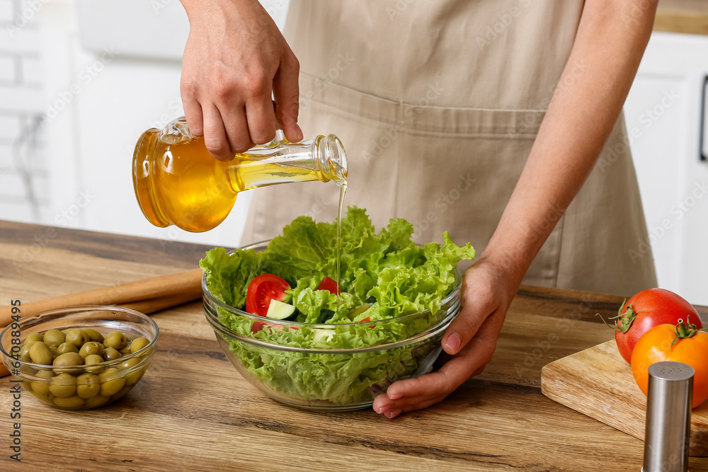 Woman adding olive oil into bowl with tasty salad at table in kitchen