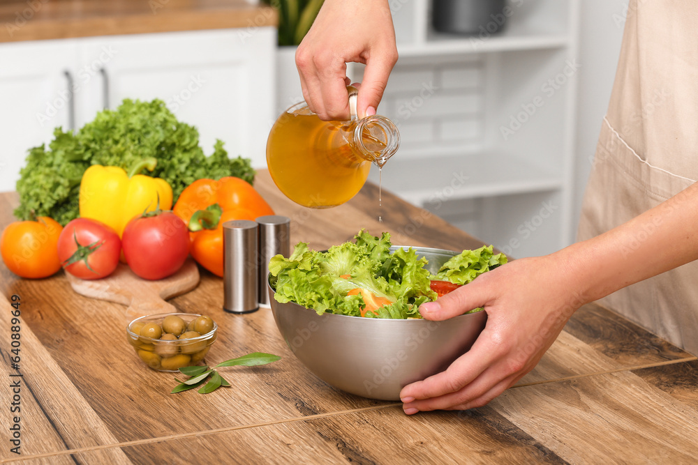 Woman adding olive oil into bowl with tasty salad at table in kitchen