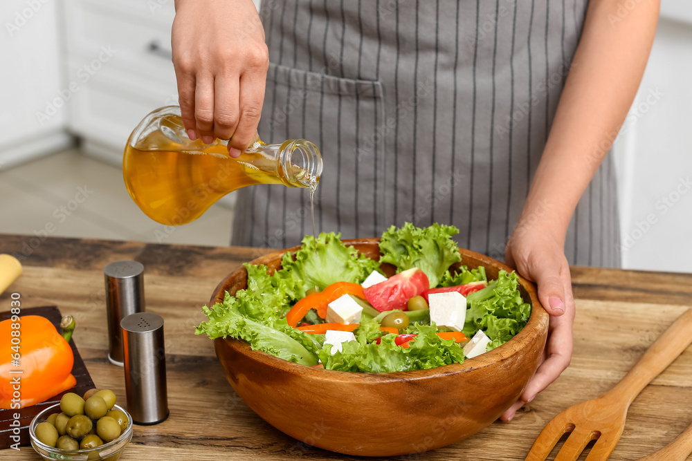 Woman adding olive oil into bowl with tasty salad at table in kitchen