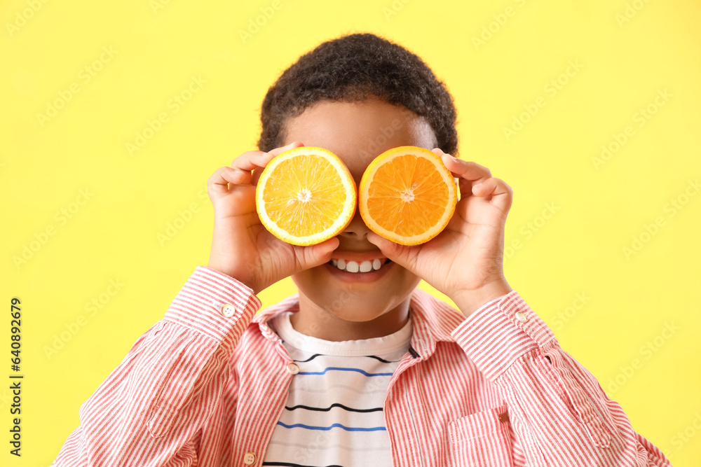 Little African-American boy with slices of orange on yellow background