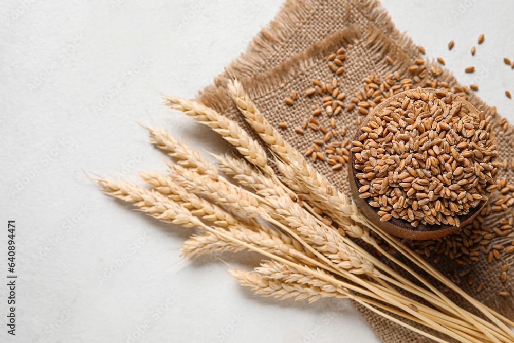 Wooden bowl with grains, wheat ears and fabric on white background