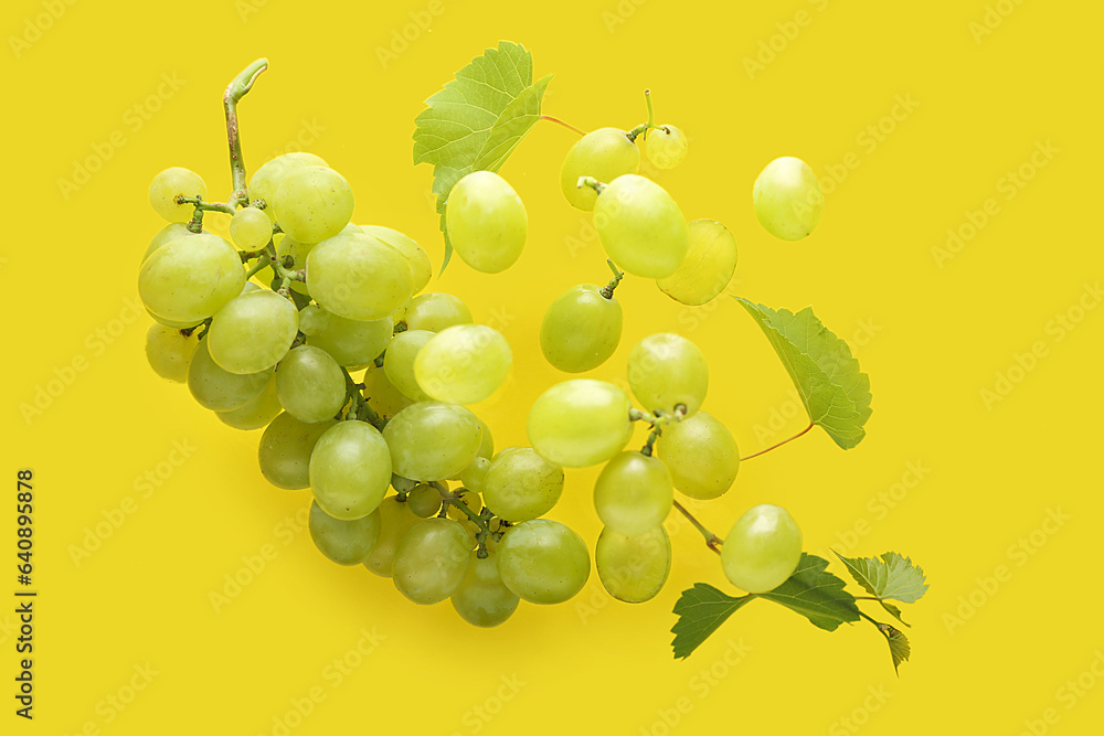 Flying sweet green grapes with leaves on yellow background