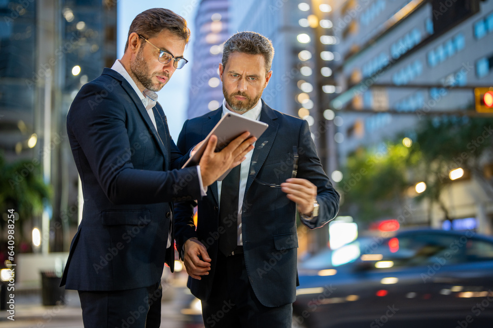 Business men check their emails and review important documents on tablet on night city background. T