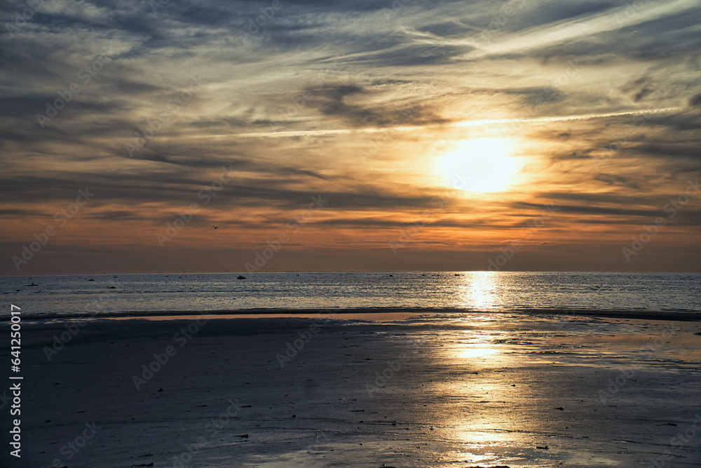 Sunset, illuminated sea. Sandy beach in the foreground. Light waves. Baltic Sea