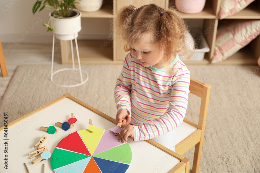 Cute little girl playing matching game with clothespins at home