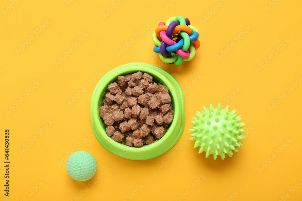 Bowl of wet pet food and balls on color background