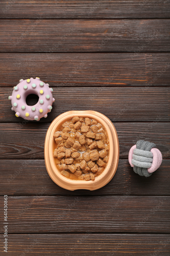 Bowl of wet pet food and toys on wooden background