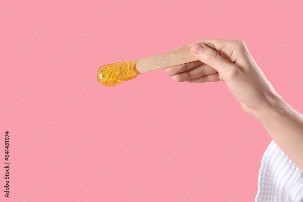 Hand holding spatula with sugaring paste on pink background