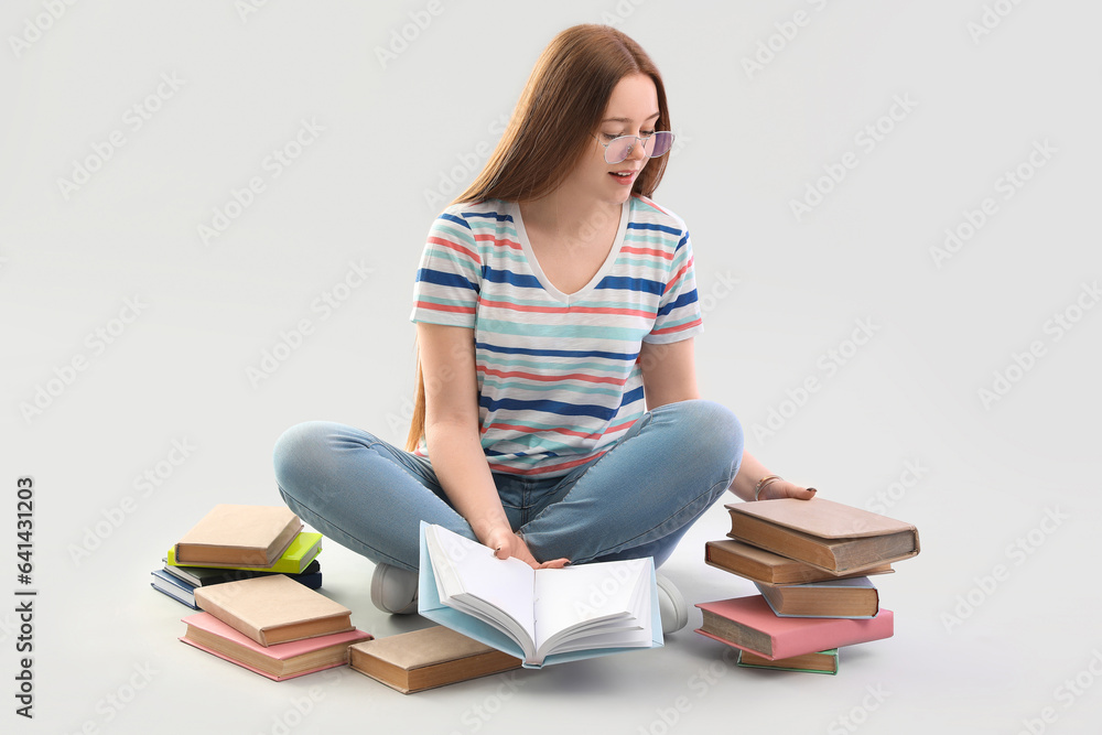 Teenage girl with books sitting on light background