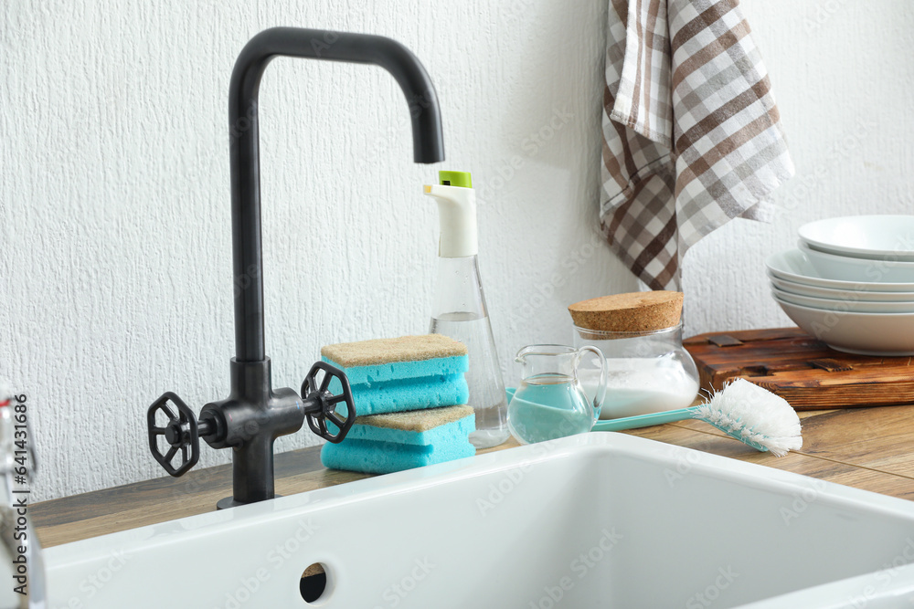 Bottle of vinegar, baking soda, brush and sponges on table near sink