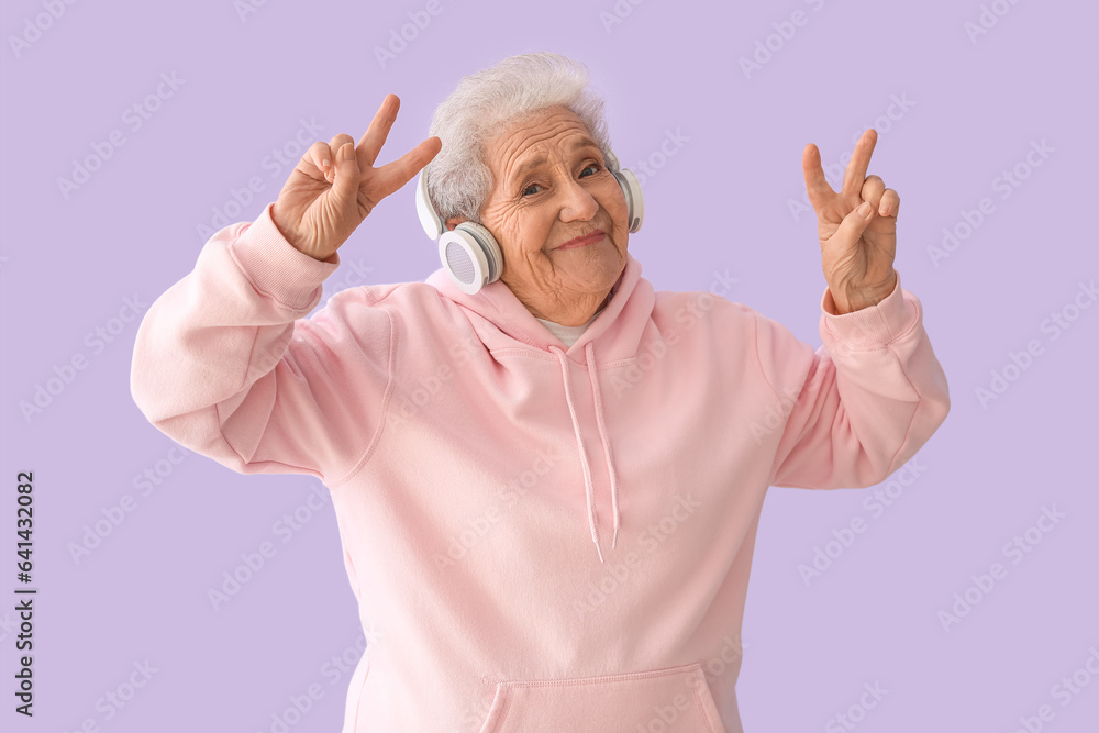 Senior woman in headphones dancing on lilac background