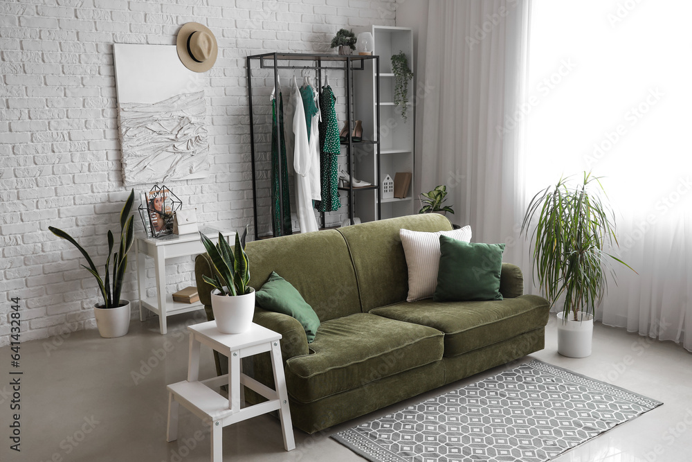 Interior of light room with sofa, shelving unit and clothes