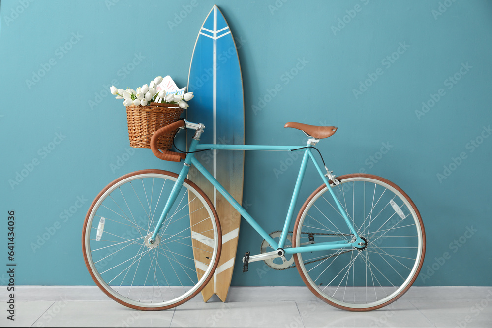 Bicycle with flowers and surfboard near blue wall in room