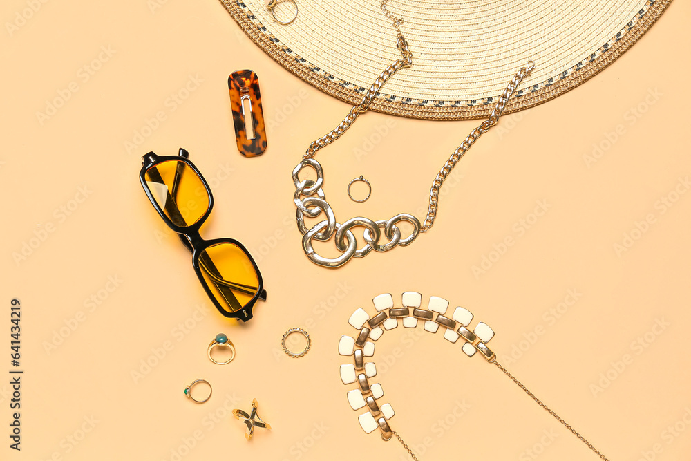 Stylish jewelry with sunglasses and summer hat on beige background