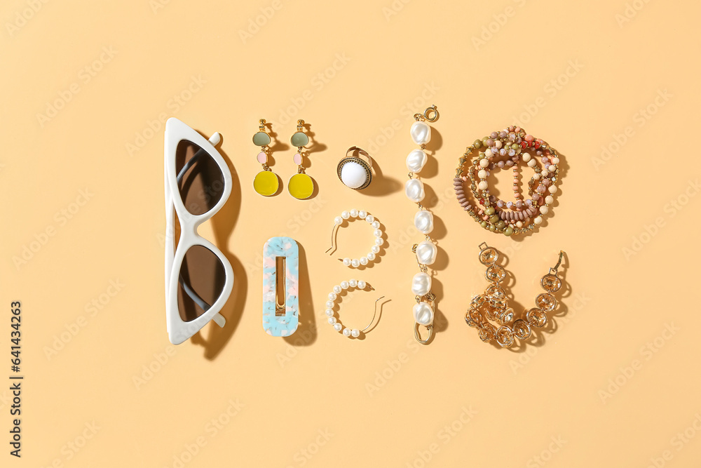 Stylish jewelry with sunglasses on beige background