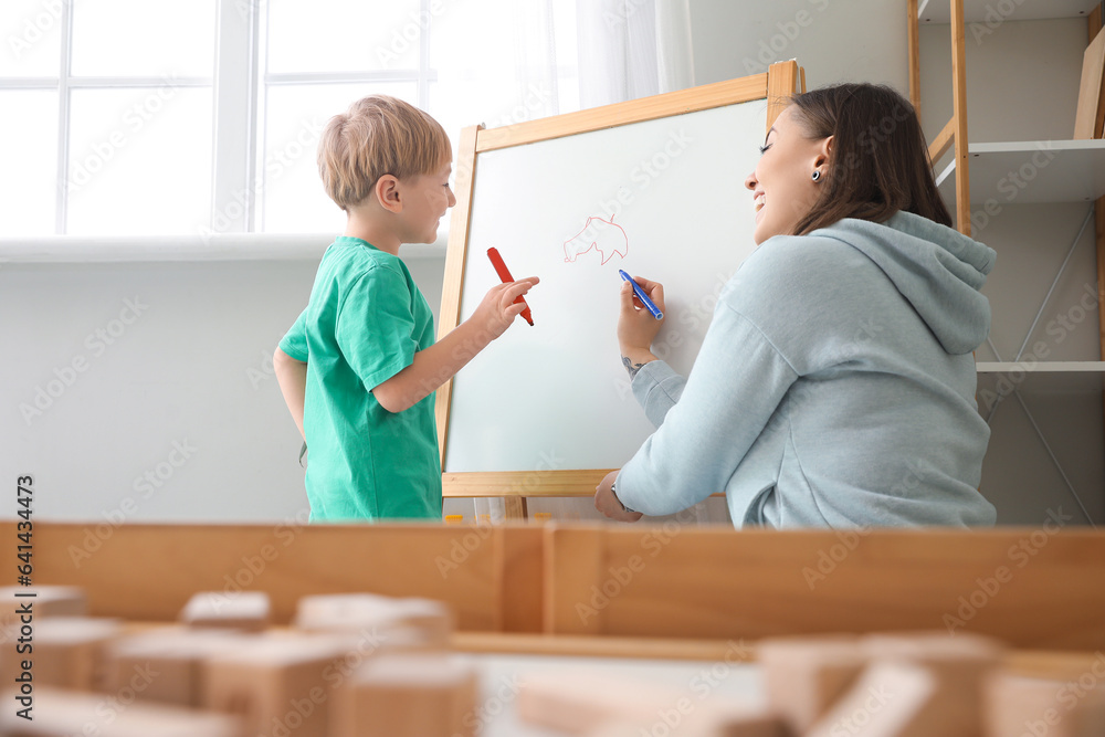 Little boy with nanny drawing on board at home