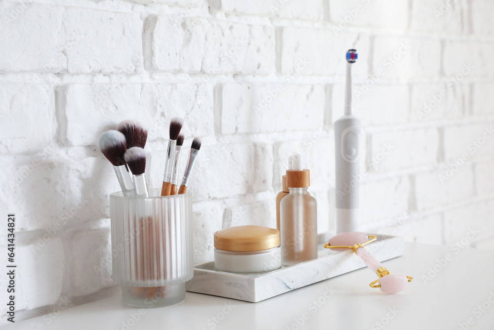 Bath accessories with makeup brushes on table near white brick wall