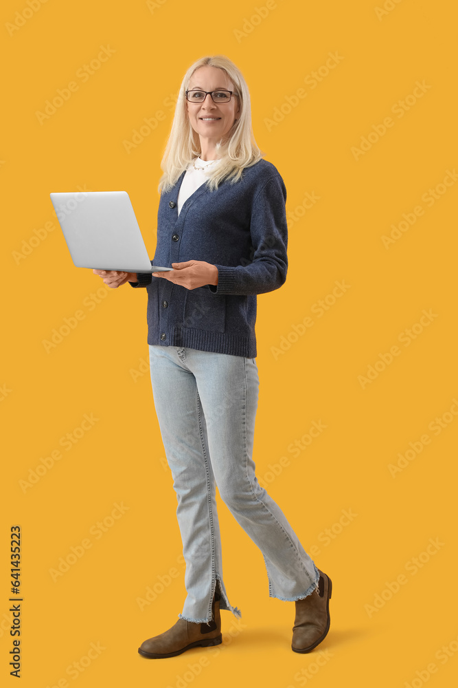 Mature female programmer working with laptop on yellow background