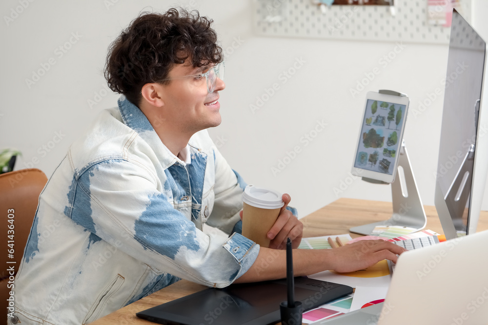 Male graphic designer with cup of coffee working at table in office