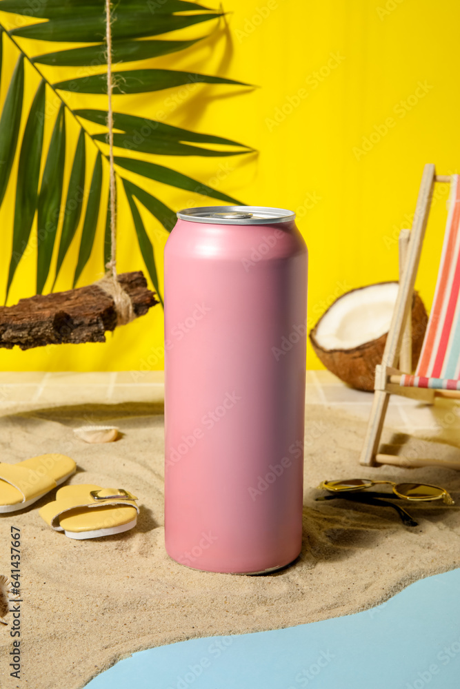 Can of soda with beach decor on sand near yellow wall