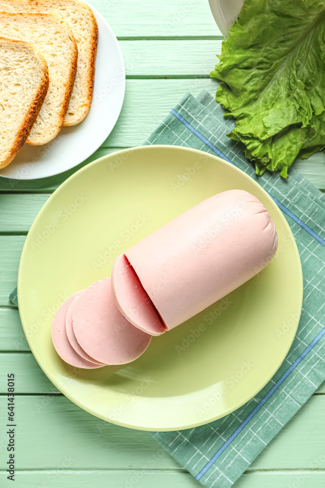 Plate with tasty boiled sausage on green wooden background