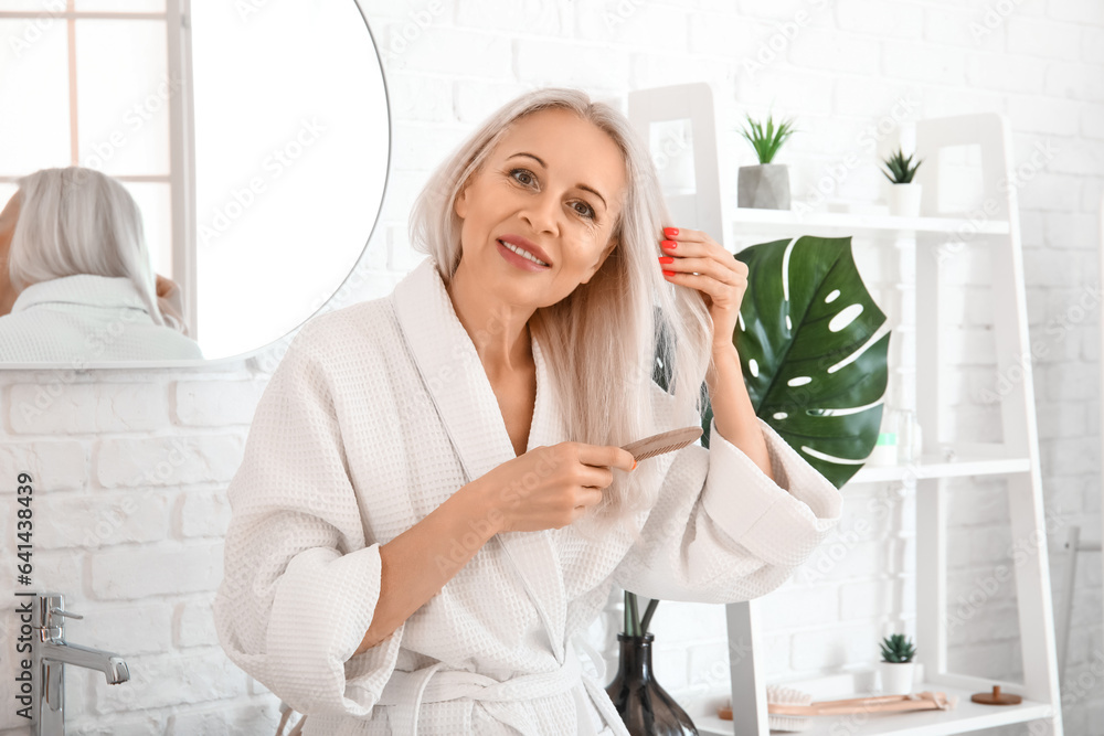 Mature blonde woman brushing hair in bathroom