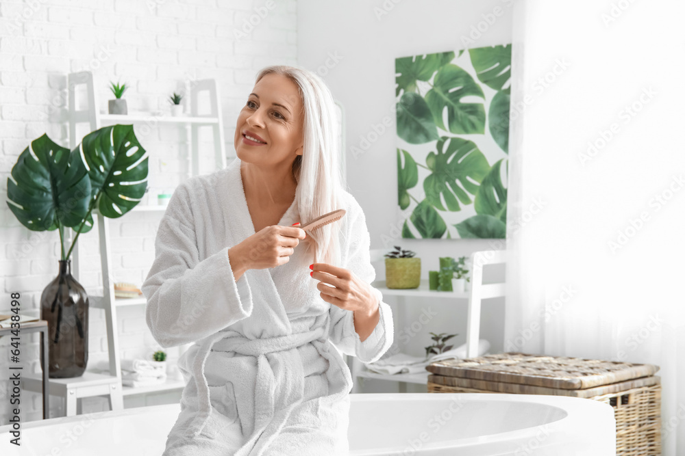 Mature blonde woman brushing hair in bathroom