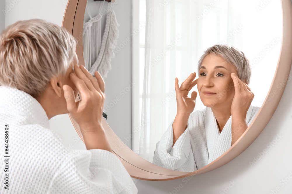 Mature woman massaging her face near mirror in bathroom