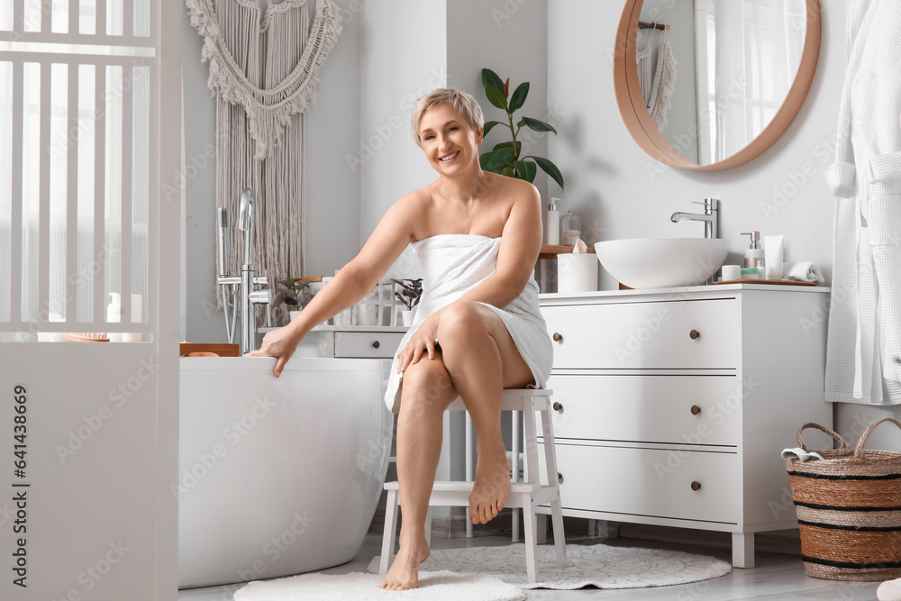 Mature woman sitting on stool after shower in bathroom