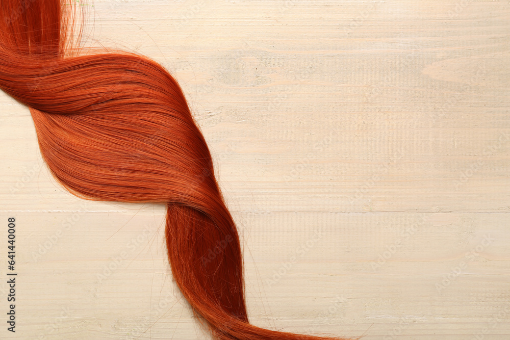 Ginger hair strand on light wooden background, closeup