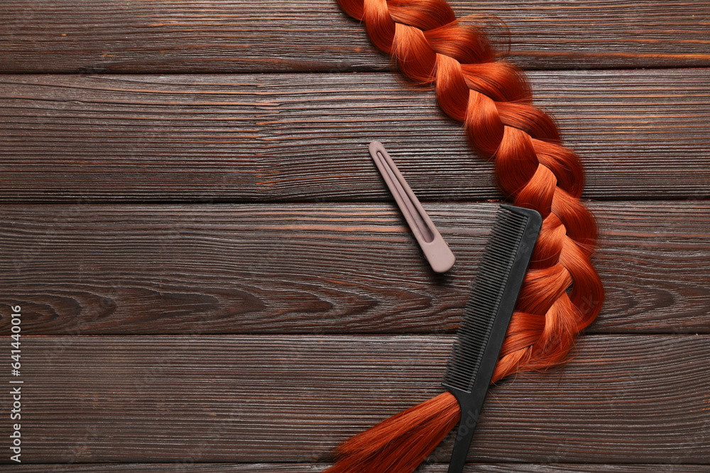 Braided ginger hair, comb and clip on wooden background