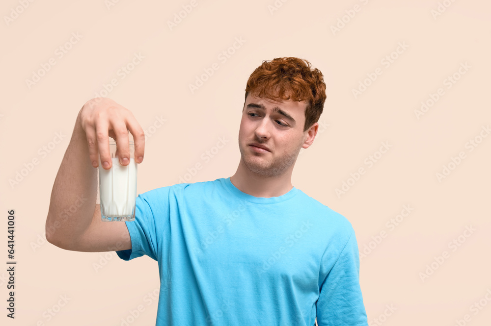 Displeased young man with glass of milk on beige background