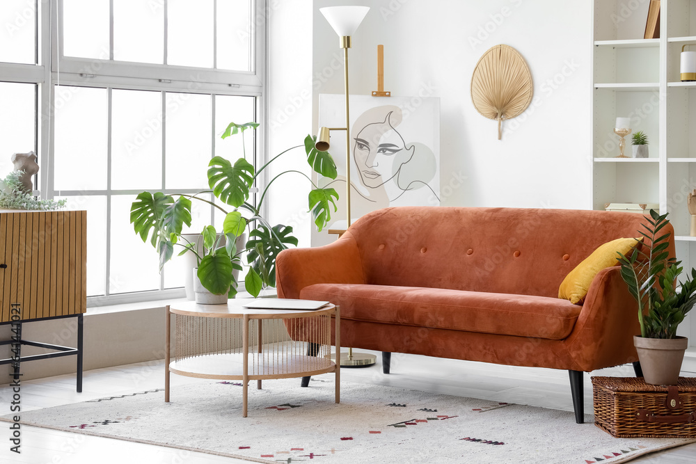 Interior of light living room with cozy brown sofa and coffee table near big window