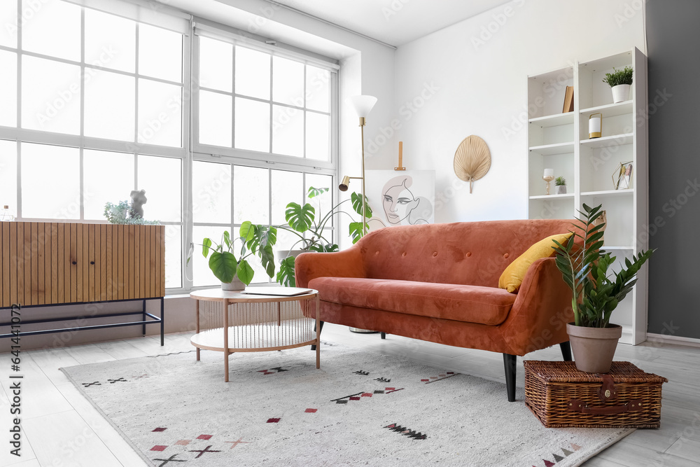 Interior of light living room with brown sofa and coffee table near big window